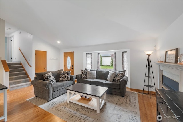 living area with vaulted ceiling, light wood-style flooring, stairway, and a fireplace