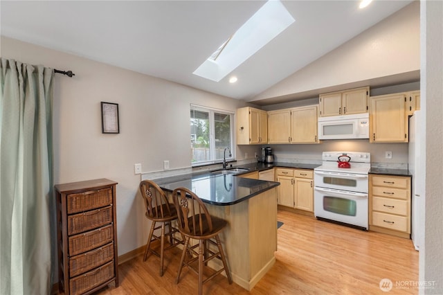 kitchen with white appliances, a sink, a skylight, vaulted ceiling, and a peninsula