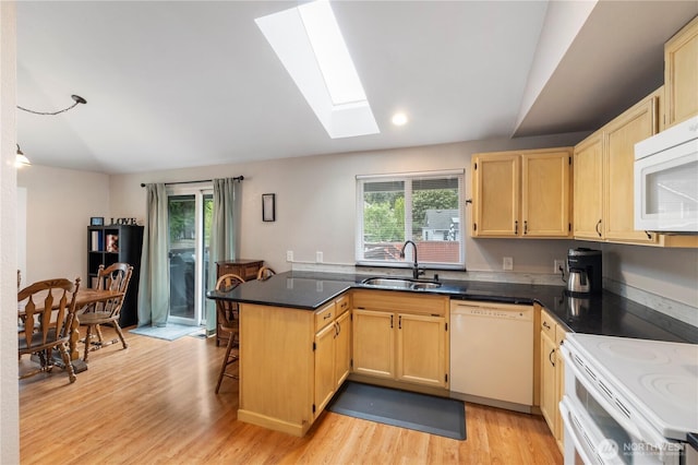 kitchen featuring white appliances, a sink, light brown cabinets, a peninsula, and a skylight