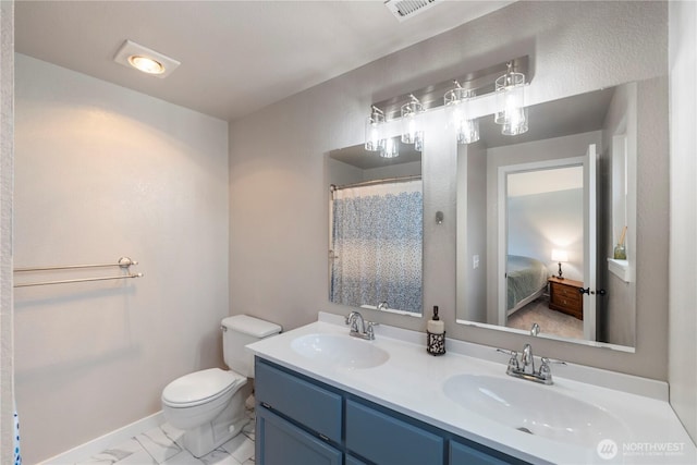 ensuite bathroom featuring toilet, marble finish flooring, double vanity, and baseboards