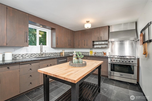 kitchen with dark countertops, appliances with stainless steel finishes, a sink, and wall chimney exhaust hood