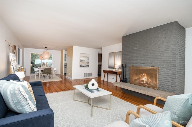 living area with baseboards, a brick fireplace, wood finished floors, and visible vents