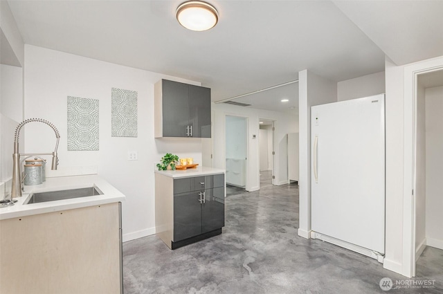 kitchen featuring a sink, finished concrete flooring, light countertops, gray cabinets, and freestanding refrigerator