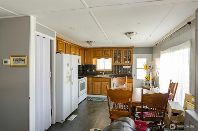 kitchen with brown cabinetry, a sink, white appliances, and plenty of natural light