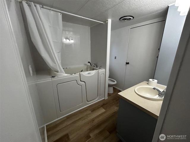 bathroom featuring wood finished floors, vanity, shower / tub combo with curtain, toilet, and visible vents
