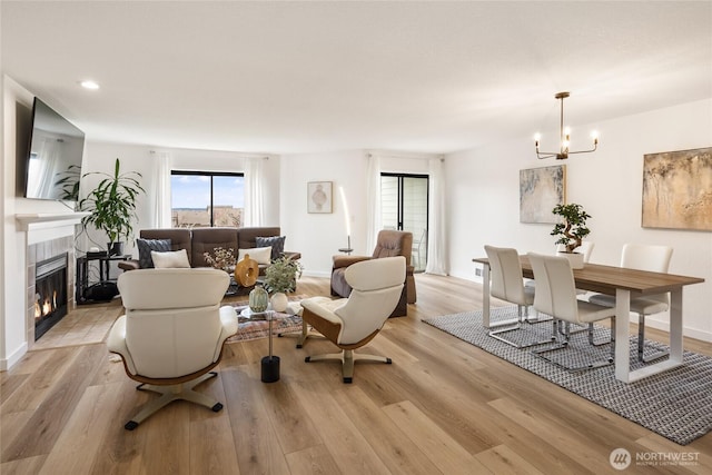 living room with a chandelier, light wood-type flooring, a tiled fireplace, and recessed lighting