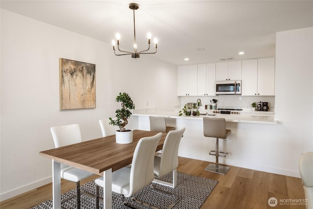dining space with an inviting chandelier, light wood finished floors, baseboards, visible vents, and recessed lighting