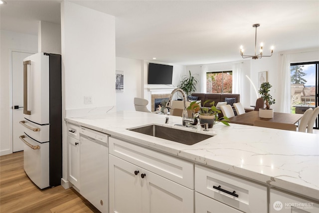 kitchen with light wood finished floors, a sink, open floor plan, a notable chandelier, and white appliances