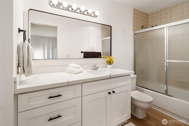 bathroom featuring toilet, vanity, wood finished floors, and combined bath / shower with glass door
