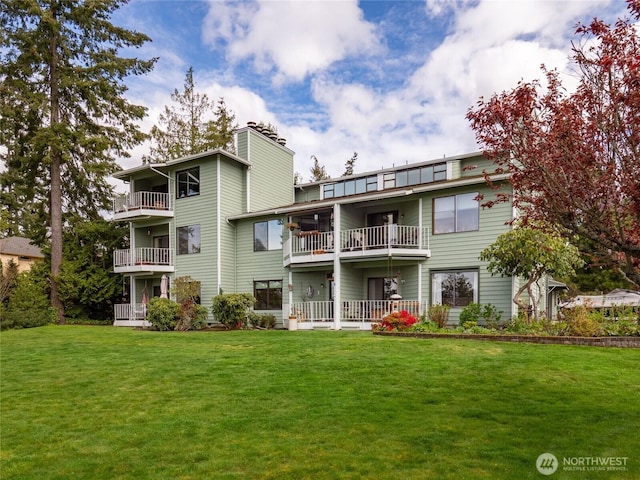 back of property featuring a lawn, a chimney, and a balcony