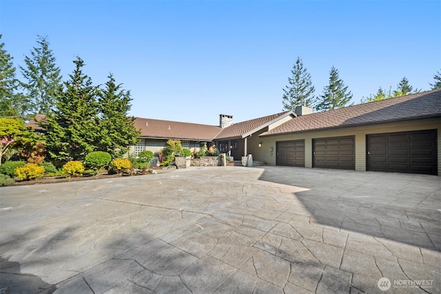 ranch-style home with a chimney, concrete driveway, and an attached garage
