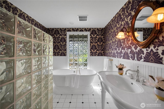 full bath featuring a soaking tub, wallpapered walls, visible vents, and wainscoting