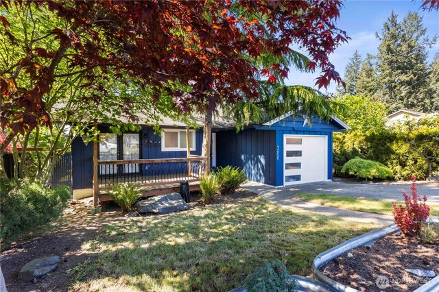 obstructed view of property with board and batten siding, driveway, an attached garage, a front lawn, and a wooden deck