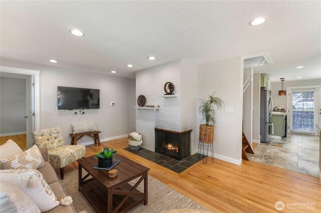 living room featuring baseboards, a fireplace, a textured ceiling, recessed lighting, and light wood-style flooring