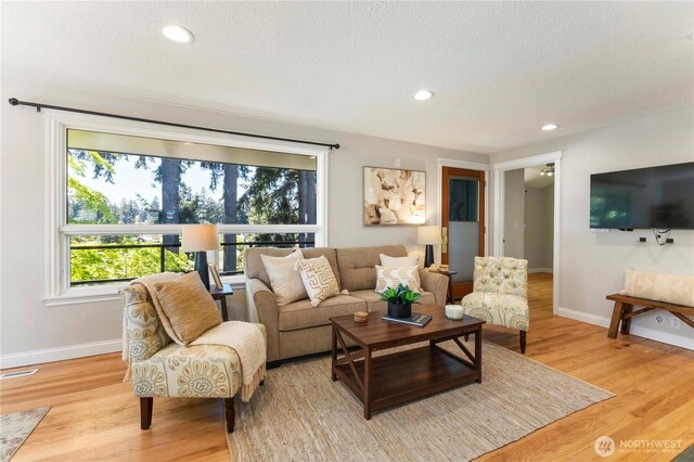 living room featuring baseboards, light wood-style flooring, a textured ceiling, and recessed lighting