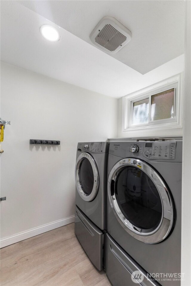 clothes washing area with washer and dryer, light wood finished floors, and baseboards