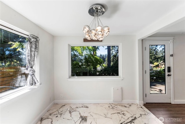 unfurnished dining area featuring healthy amount of natural light, a chandelier, marble look tile flooring, and baseboards