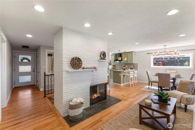 living room featuring baseboards, a textured ceiling, light wood-style floors, a brick fireplace, and recessed lighting