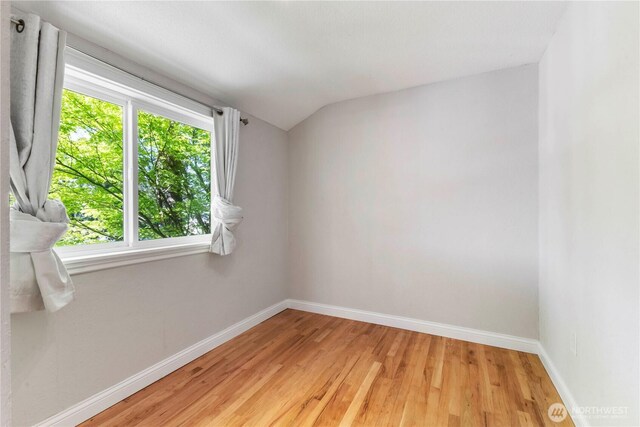 empty room featuring baseboards, lofted ceiling, and light wood-style floors