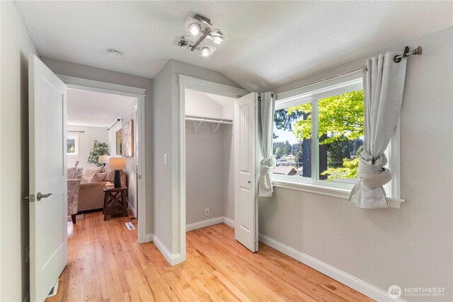 bedroom featuring light wood-type flooring, lofted ceiling, baseboards, and a closet