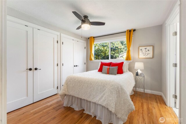 bedroom featuring two closets, light wood finished floors, baseboards, and a ceiling fan