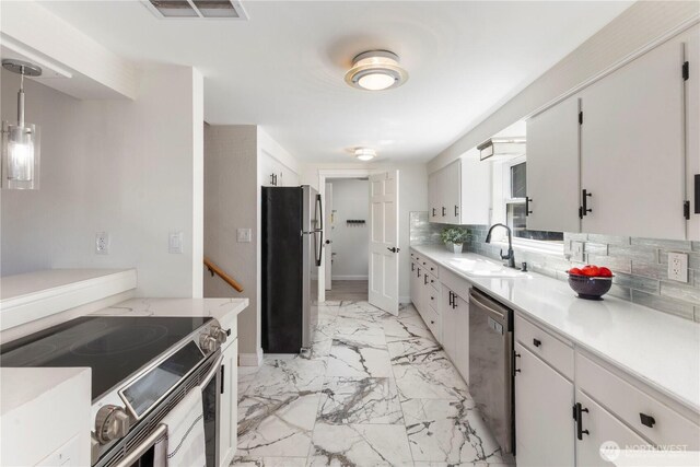 kitchen featuring a sink, appliances with stainless steel finishes, light marble finish floors, light countertops, and decorative backsplash