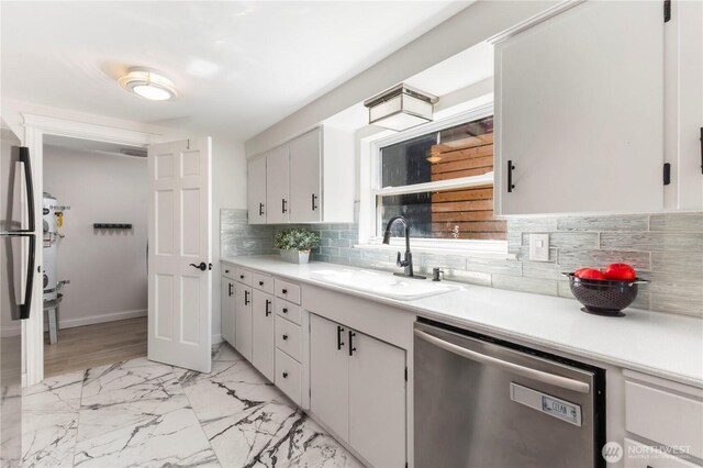 kitchen featuring appliances with stainless steel finishes, a sink, tasteful backsplash, light countertops, and light marble finish flooring