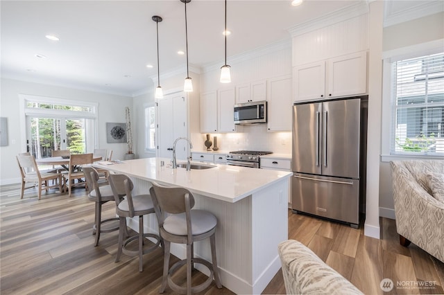 kitchen with white cabinets, a sink, light wood-type flooring, high quality appliances, and tasteful backsplash