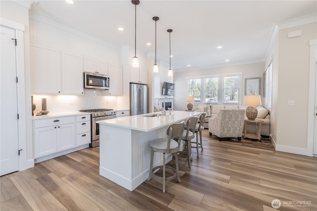 kitchen with a sink, light wood-type flooring, open floor plan, a kitchen bar, and appliances with stainless steel finishes
