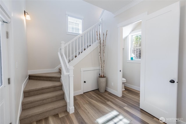 stairs with baseboards, wood finished floors, and crown molding