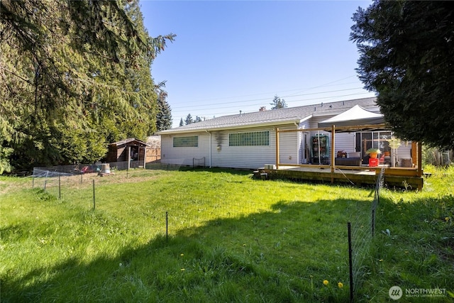 rear view of property featuring fence, a deck, a yard, and a gazebo