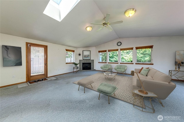carpeted living area featuring baseboards, ceiling fan, vaulted ceiling with skylight, and a tile fireplace