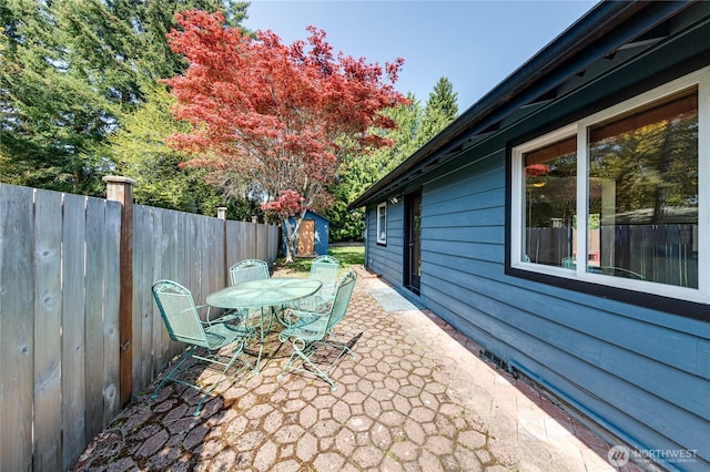view of patio / terrace featuring a storage shed, fence, outdoor dining area, and an outdoor structure