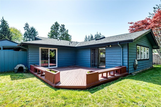 rear view of house with a lawn, a shingled roof, a wooden deck, and fence