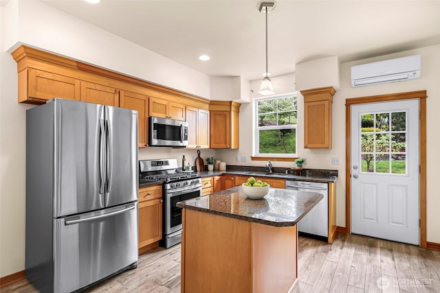 kitchen featuring appliances with stainless steel finishes, a wall unit AC, a center island, dark stone counters, and light wood-type flooring