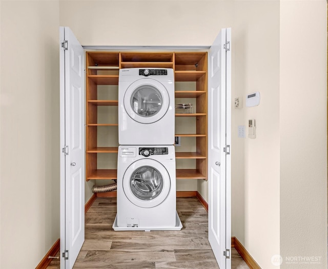 washroom featuring stacked washer and clothes dryer, wood finished floors, and baseboards