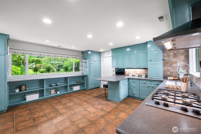 kitchen with wall chimney range hood, a peninsula, stainless steel gas cooktop, backsplash, and a sink