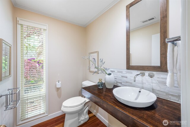 half bathroom featuring a sink, decorative backsplash, toilet, crown molding, and wood finished floors