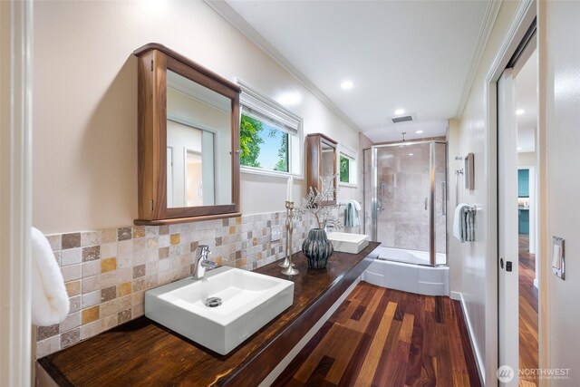 bathroom featuring a stall shower, wood finished floors, ornamental molding, backsplash, and double vanity