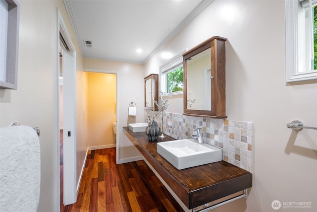 bathroom with wood finished floors, decorative backsplash, ornamental molding, toilet, and double vanity