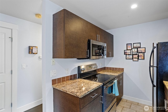 kitchen with appliances with stainless steel finishes, baseboards, dark brown cabinetry, and light stone countertops