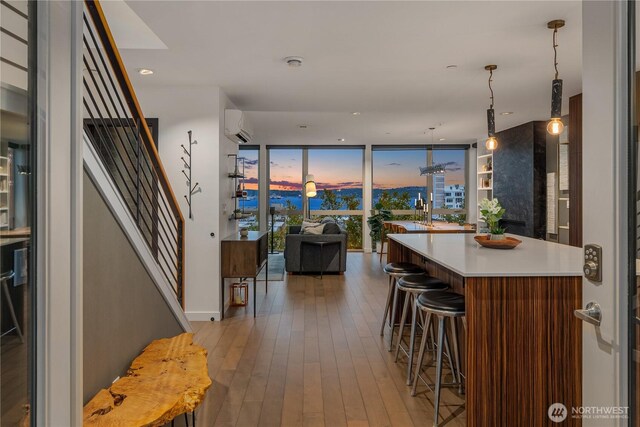 kitchen with floor to ceiling windows, a breakfast bar area, a wall mounted air conditioner, light countertops, and hardwood / wood-style floors