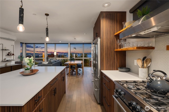 kitchen with wall chimney range hood, a wall of windows, light wood-style floors, light countertops, and stainless steel appliances