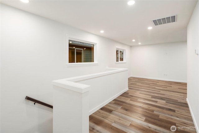 hall with recessed lighting, wood finished floors, visible vents, and an upstairs landing
