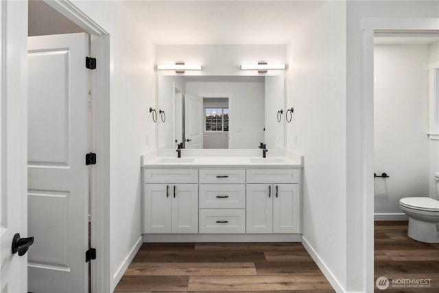 full bath featuring double vanity, wood finished floors, toilet, a sink, and baseboards