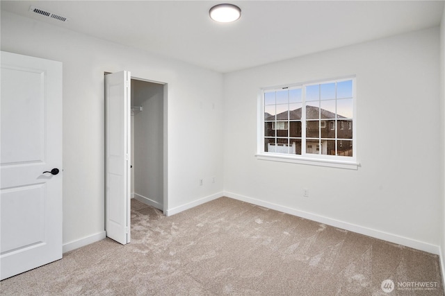 unfurnished bedroom featuring a closet, a walk in closet, baseboards, carpet flooring, and visible vents