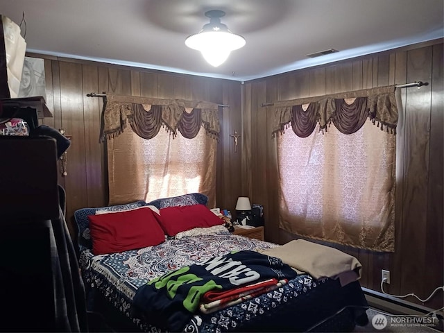bedroom with wooden walls, ceiling fan, and visible vents