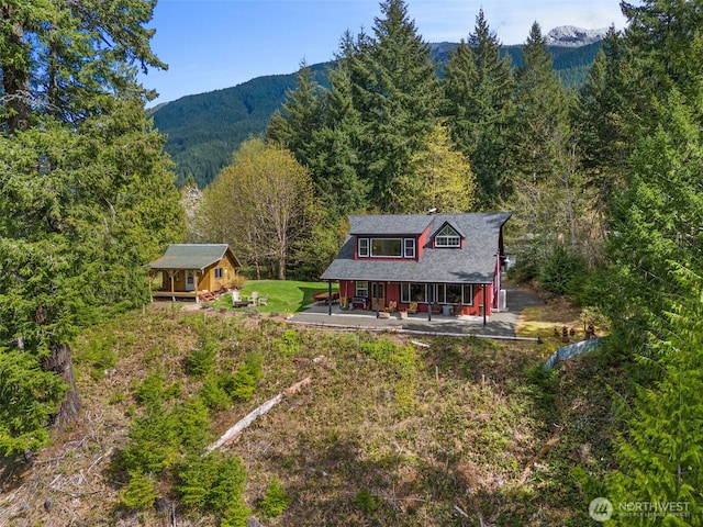rear view of property featuring a porch, a mountain view, an outbuilding, and a wooded view