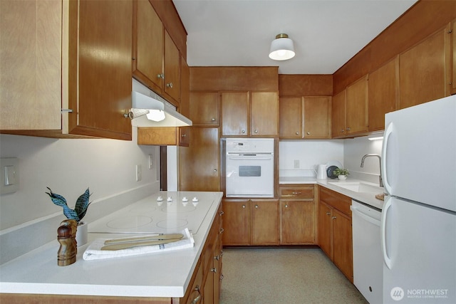 kitchen with white appliances, under cabinet range hood, a sink, and light countertops