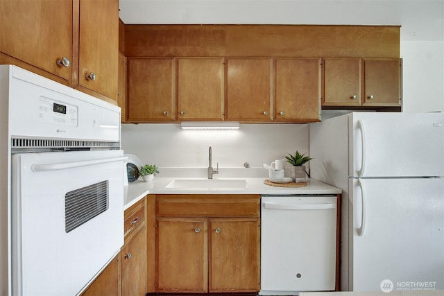 kitchen with white appliances, brown cabinets, a sink, and light countertops